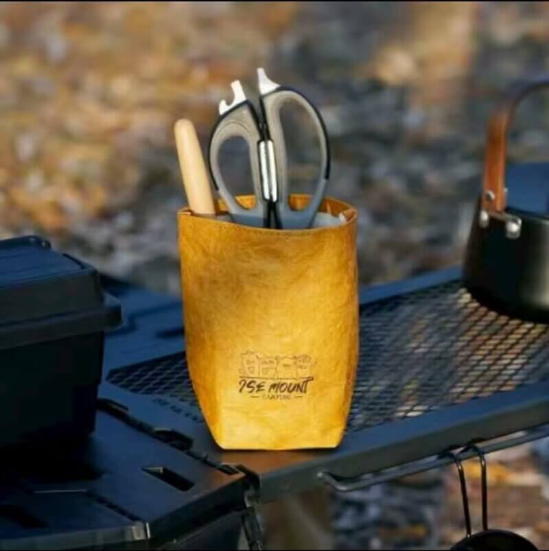 An Orange Water-proof Kraft Paper Storage Organizer Holding tools on a Camping Table